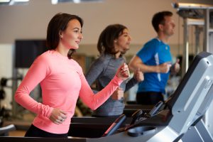 Woman and two young adults running on treadmills at a gym